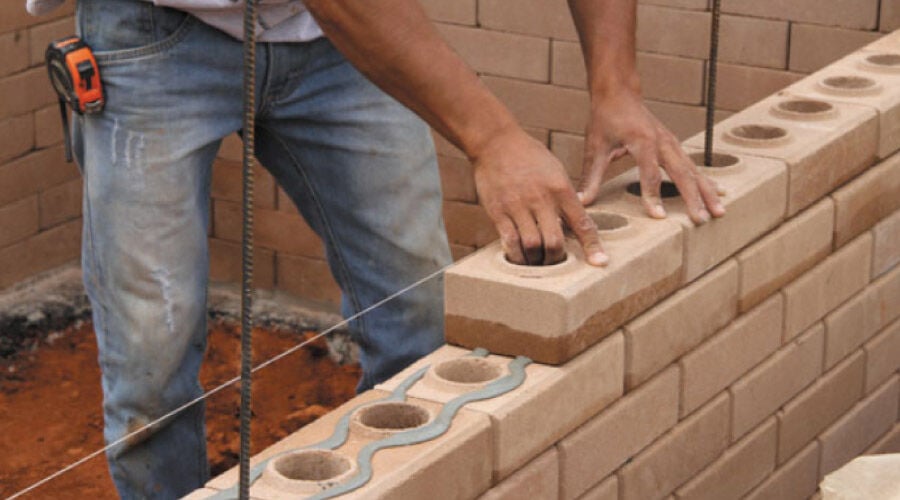 Homem construindo parede com tijolo ecológico.